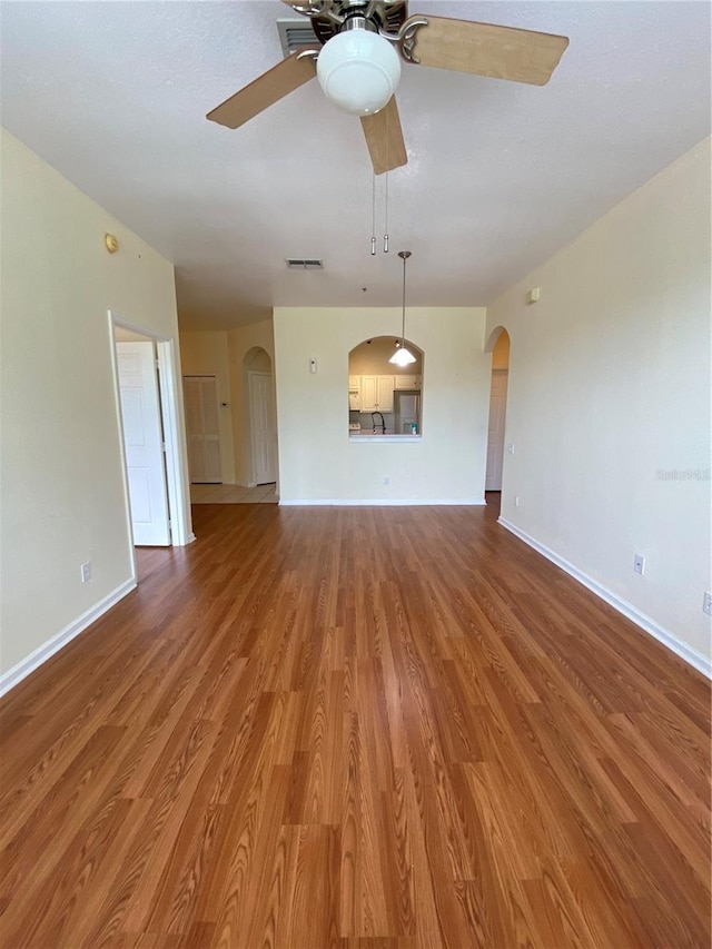 unfurnished living room with wood finished floors, visible vents, arched walkways, baseboards, and ceiling fan