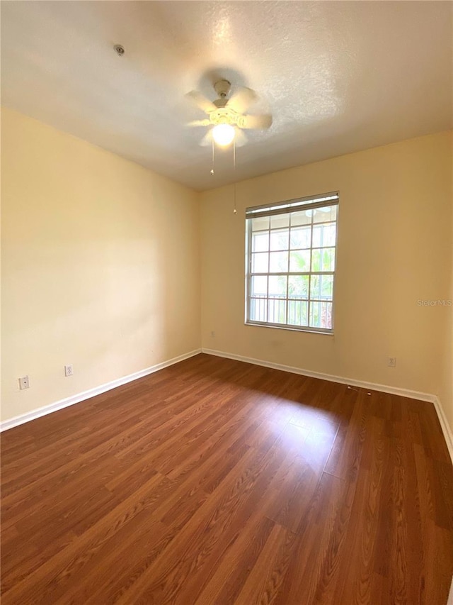 spare room featuring a ceiling fan, baseboards, and dark wood finished floors
