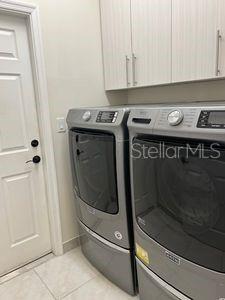 5060 Arancia Ln, Ave Maria, FL 34142 - clothes washing area with light tile patterned floors, cabinet space, and washing machine and clothes dryer