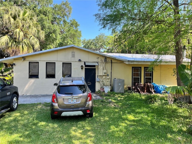 view of front of house with stucco siding, central AC, a front yard, and metal roof