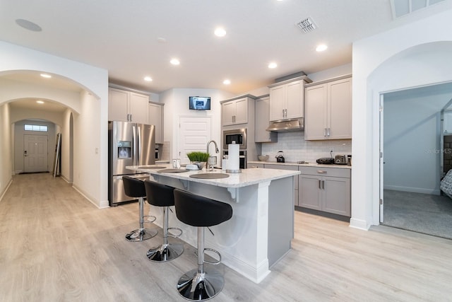 kitchen with a kitchen breakfast bar, stainless steel appliances, under cabinet range hood, gray cabinetry, and visible vents