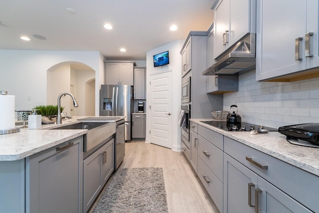 kitchen featuring under cabinet range hood, a sink, stainless steel appliances, and gray cabinetry