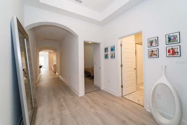 corridor with light wood-style flooring, baseboards, and arched walkways