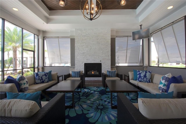 living room featuring wood ceiling, a stone fireplace, an inviting chandelier, and a raised ceiling