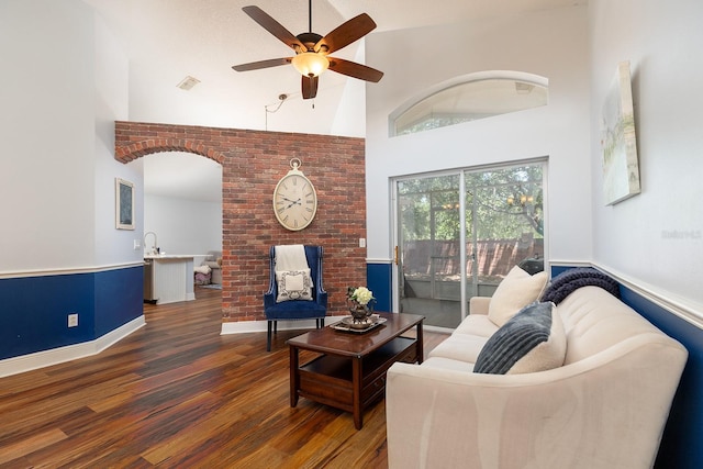 living area with a ceiling fan, visible vents, wood finished floors, and a towering ceiling