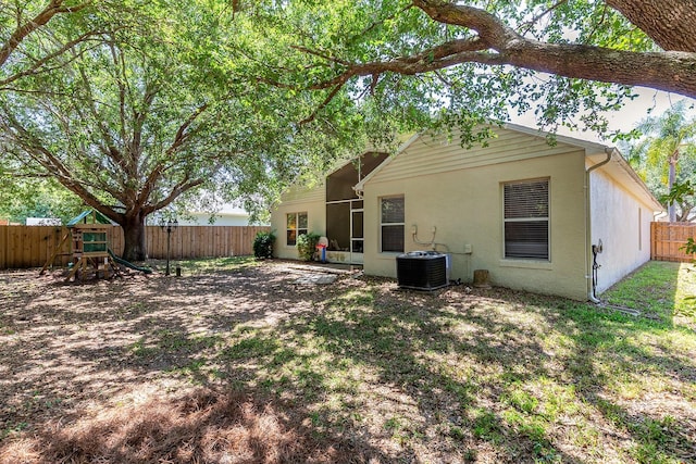 rear view of house featuring stucco siding, a fenced backyard, a playground, and central AC