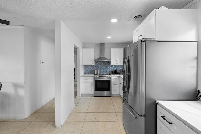 kitchen with a textured ceiling, light tile patterned flooring, stainless steel appliances, white cabinets, and wall chimney exhaust hood