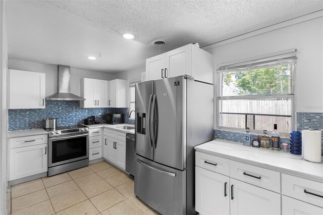kitchen featuring wall chimney range hood, a sink, decorative backsplash, stainless steel appliances, and white cabinetry