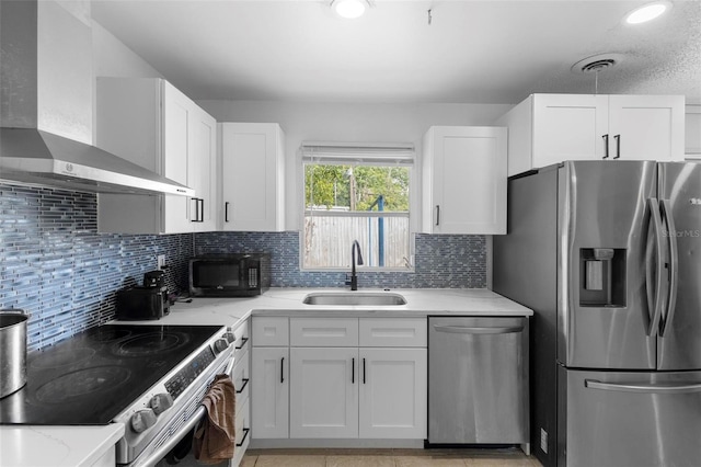kitchen with wall chimney range hood, appliances with stainless steel finishes, white cabinetry, and a sink
