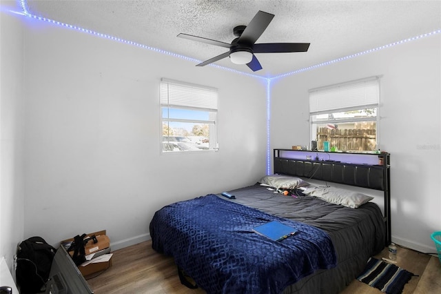 bedroom featuring baseboards, a ceiling fan, wood finished floors, and a textured ceiling
