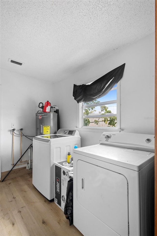 laundry room with washing machine and clothes dryer, light wood-style flooring, a textured ceiling, electric water heater, and laundry area