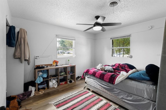 bedroom with ceiling fan, visible vents, wood finished floors, and a textured ceiling