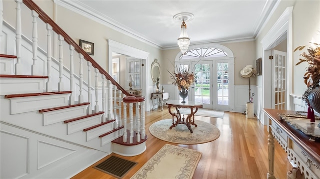 entrance foyer featuring light wood-style flooring, crown molding, visible vents, a decorative wall, and stairs