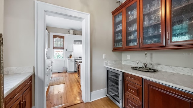bar featuring wine cooler, a bar, baseboards, and light wood finished floors