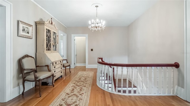 hall with an inviting chandelier, light wood finished floors, baseboards, and an upstairs landing