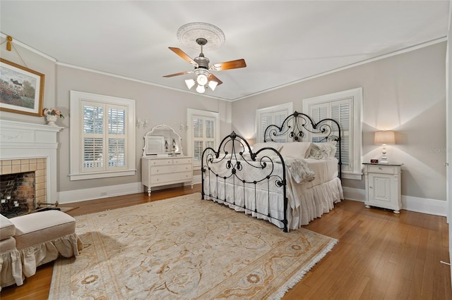 bedroom with a fireplace, crown molding, baseboards, and wood finished floors