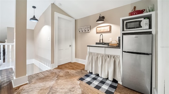 bar with freestanding refrigerator, baseboards, a sink, white microwave, and vaulted ceiling