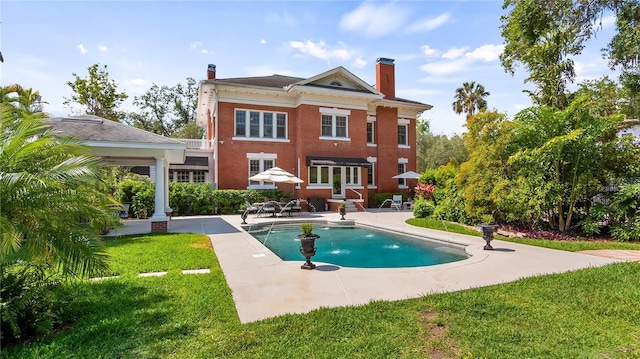 back of property with a chimney, a yard, a patio, and brick siding