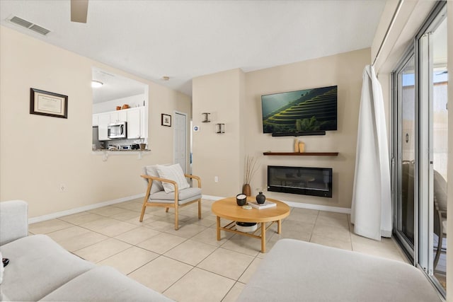 living room featuring light tile patterned floors, visible vents, baseboards, and a glass covered fireplace