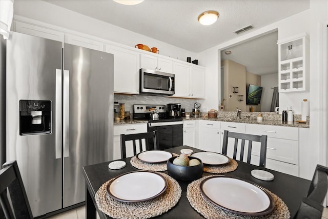 kitchen with white cabinetry, decorative backsplash, appliances with stainless steel finishes, visible vents, and stone counters