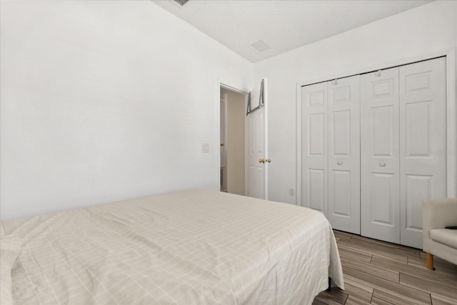 bedroom with visible vents, wood finish floors, and a closet
