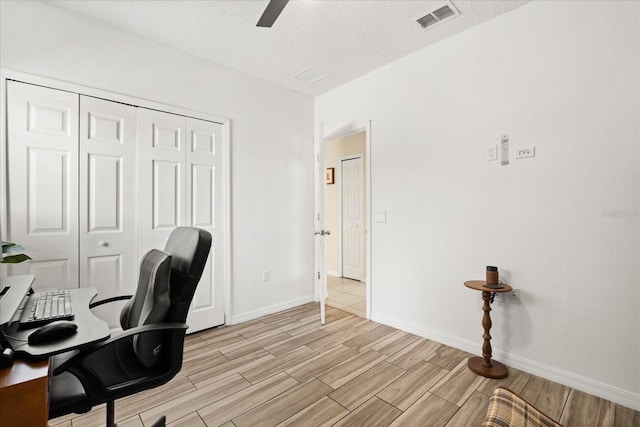 office with a textured ceiling, visible vents, light wood-style floors, baseboards, and a ceiling fan