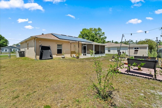 rear view of house with a fenced backyard, roof mounted solar panels, a sunroom, and a lawn