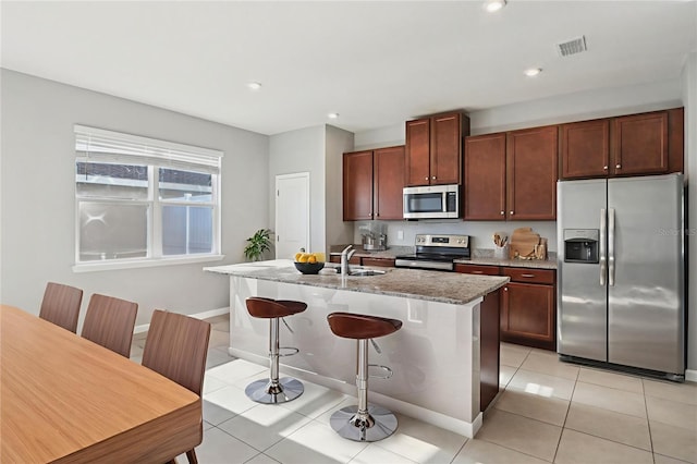 6013 Blue Lily Way, Winter Garden, FL 34787 - kitchen with appliances with stainless steel finishes, an island with sink, light stone counters, light tile patterned flooring, and a breakfast bar
