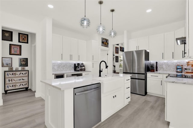 kitchen featuring a sink, light wood-style floors, decorative backsplash, light stone counters, and appliances with stainless steel finishes