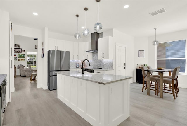 kitchen featuring tasteful backsplash, visible vents, freestanding refrigerator, wall chimney range hood, and light stone countertops