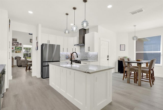 kitchen featuring backsplash, freestanding refrigerator, wall chimney range hood, and light wood finished floors