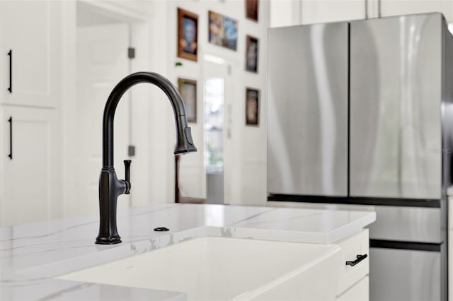 interior details featuring white cabinetry, light stone countertops, a sink, and freestanding refrigerator