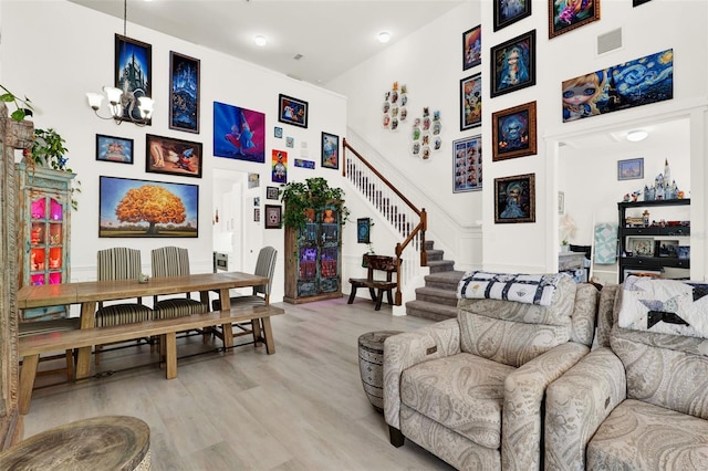 living area featuring stairs, light wood-type flooring, a high ceiling, a notable chandelier, and visible vents