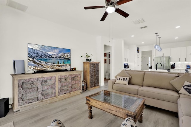 living room with a ceiling fan, visible vents, and light wood-style floors