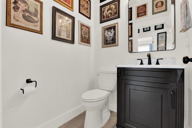 half bath with wood finished floors, vanity, toilet, and baseboards