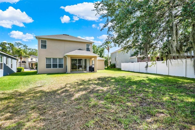 back of property with stucco siding, fence, and a yard