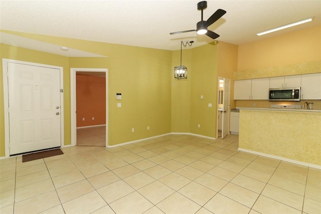 interior space with light tile patterned floors, a ceiling fan, and baseboards