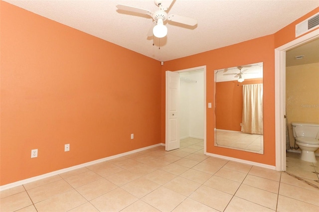 empty room with light tile patterned floors, a textured ceiling, ceiling fan, visible vents, and baseboards