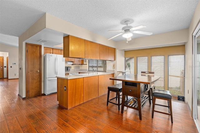 1105 Mill Run Cir, Apopka, FL 32703 - kitchen with freestanding refrigerator, a peninsula, brown cabinets, dark wood-style flooring, and a ceiling fan