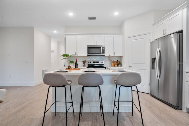 kitchen with white cabinets, a breakfast bar, visible vents, decorative backsplash, and appliances with stainless steel finishes