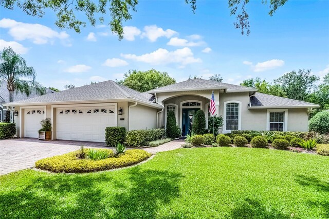 view of front of home featuring a garage, a shingled roof, a front yard, stucco siding, and decorative driveway