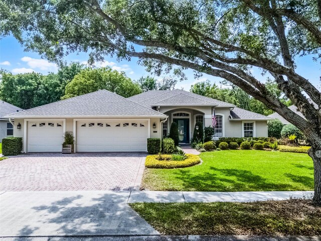 ranch-style house featuring stucco siding, a front lawn, decorative driveway, and a garage
