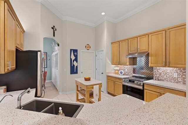 kitchen with arched walkways, a sink, appliances with stainless steel finishes, under cabinet range hood, and light tile patterned floors