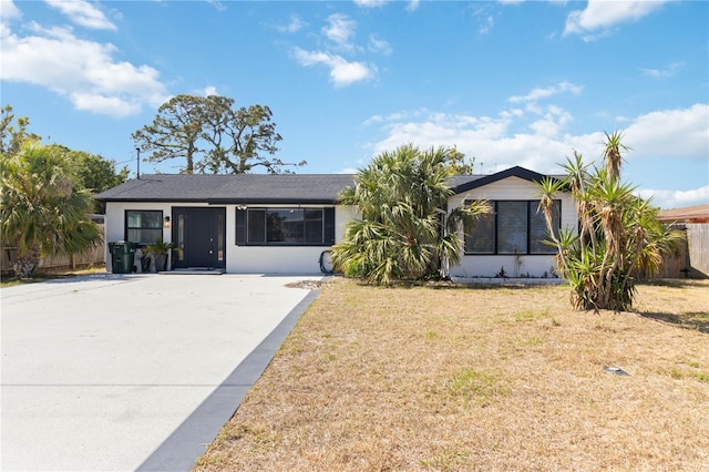 ranch-style home featuring driveway, fence, stucco siding, and a front lawn