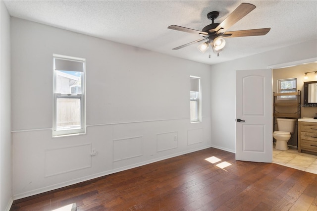 unfurnished bedroom featuring ensuite bath, a textured ceiling, light wood-style flooring, and multiple windows