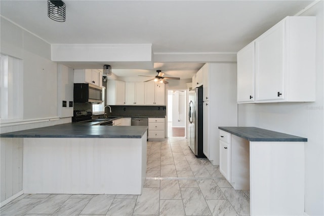 kitchen featuring appliances with stainless steel finishes, marble finish floor, dark countertops, a sink, and a peninsula
