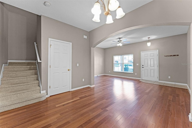 16064 Old Ash Loop, Orlando, FL 32828 - unfurnished living room featuring arched walkways, wood finished floors, baseboards, ceiling fan with notable chandelier, and stairs