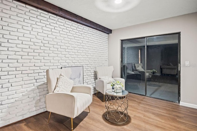sitting room featuring wood finished floors and brick wall