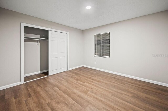 unfurnished bedroom featuring baseboards, wood finished floors, and a closet