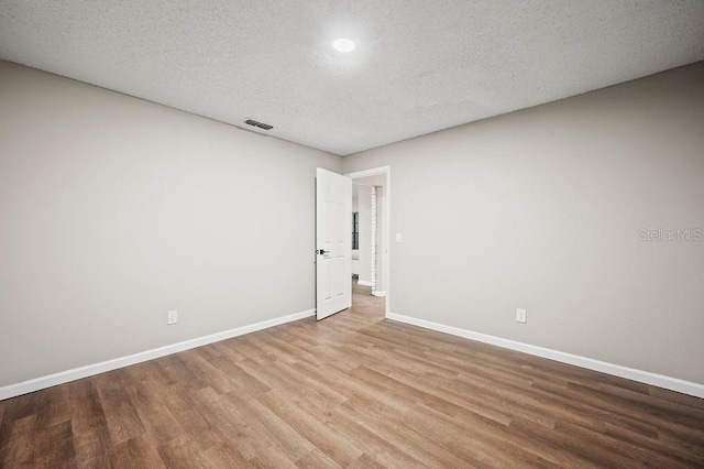 empty room with a textured ceiling, wood finished floors, and baseboards